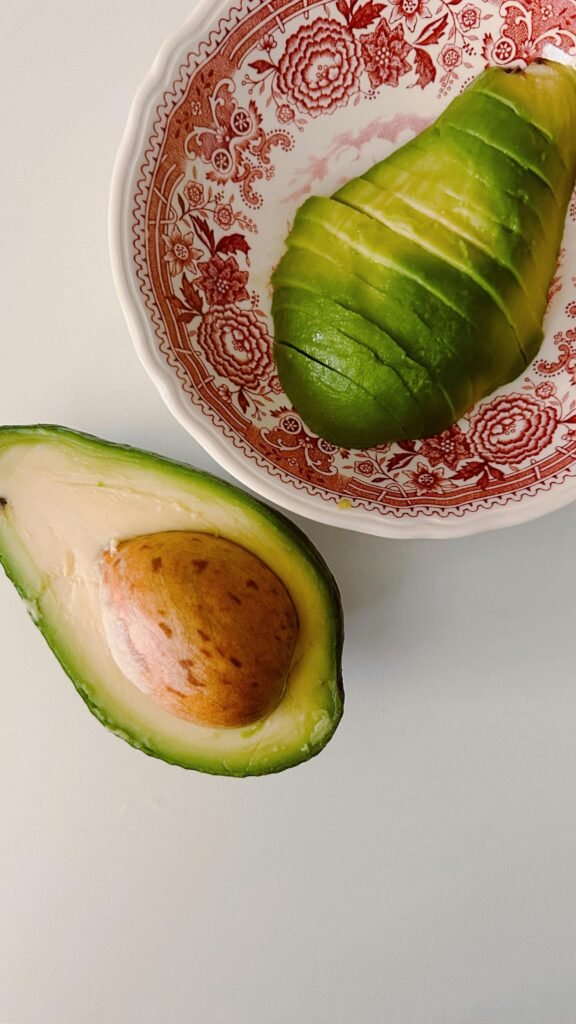 Close-up of a ripe, sliced avocado in a decorative red bowl on a white surface.